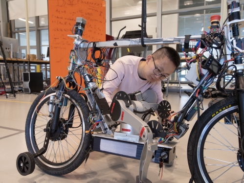 Male student wearing a light pink T-shirt works on a motorized bike in a lab setting.